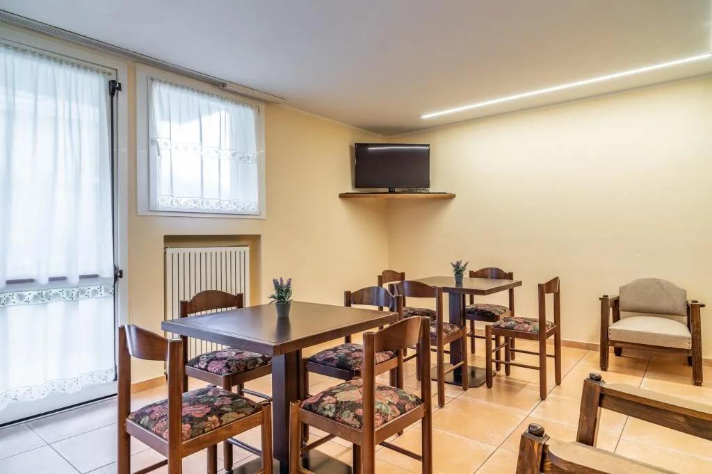 Saletta comune con tavoli in legno, sedie a fiori e televisore a parete