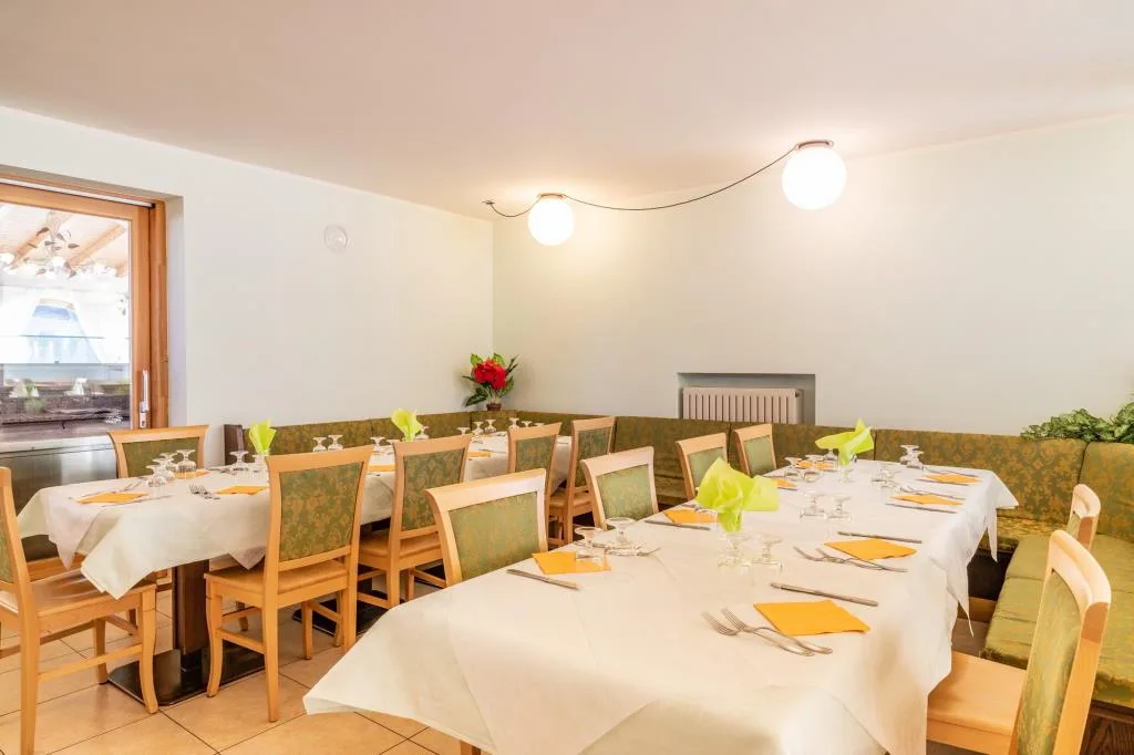 Sala da pranzo con tavoli apparecchiati, tovaglie bianche e panca verde