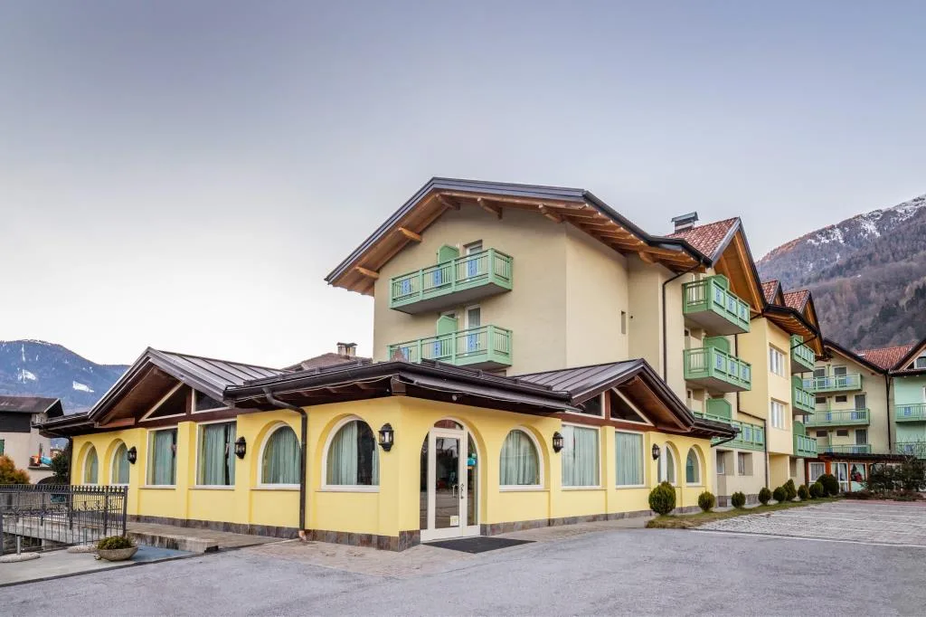 Esterno dell'hotel con facciata gialla e balconi verdi circondato dalle montagne