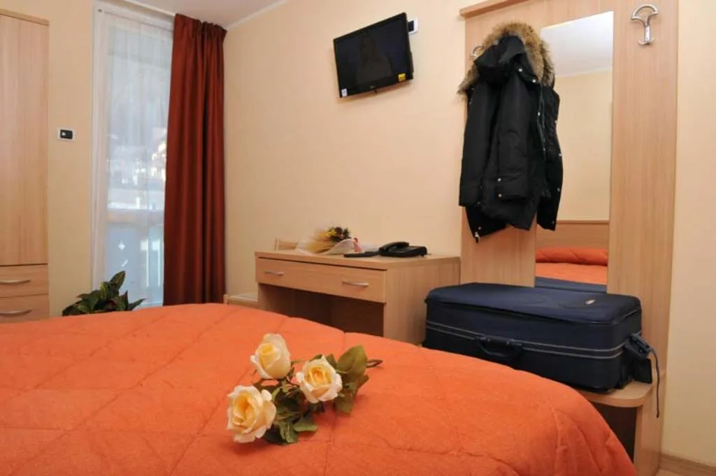 Camera da letto con copriletto arancione, scrivania, TV e specchio