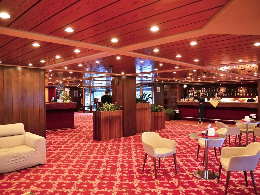 Hall dell'hotel con reception, bar, moquette rossa e soffitto in legno