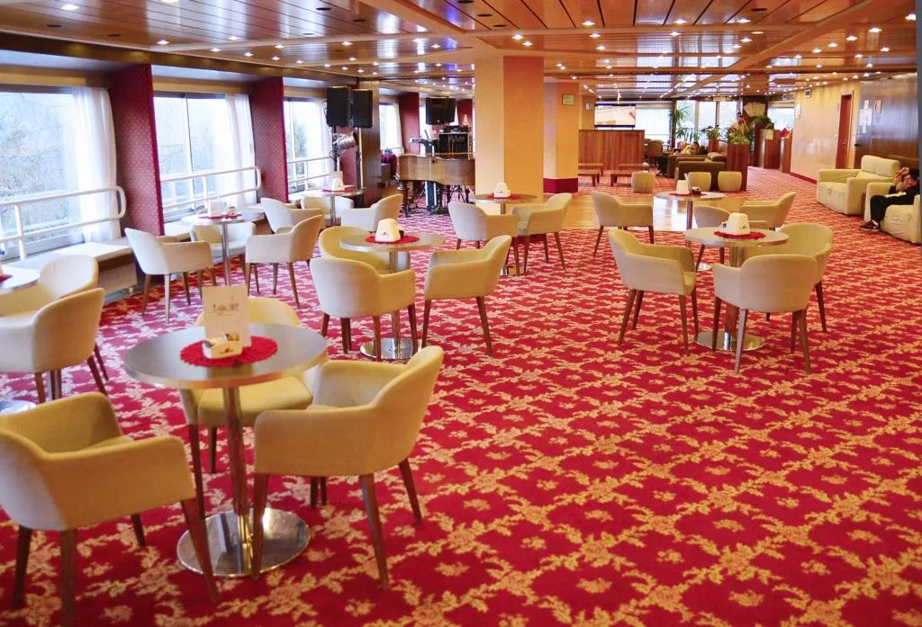 Sala lounge con tavolini, poltrone bianche e moquette rossa a motivi floreali