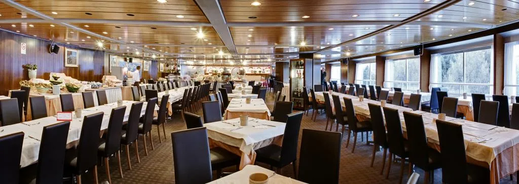 Ampia sala da pranzo con lunghe tavolate e grandi finestre panoramiche