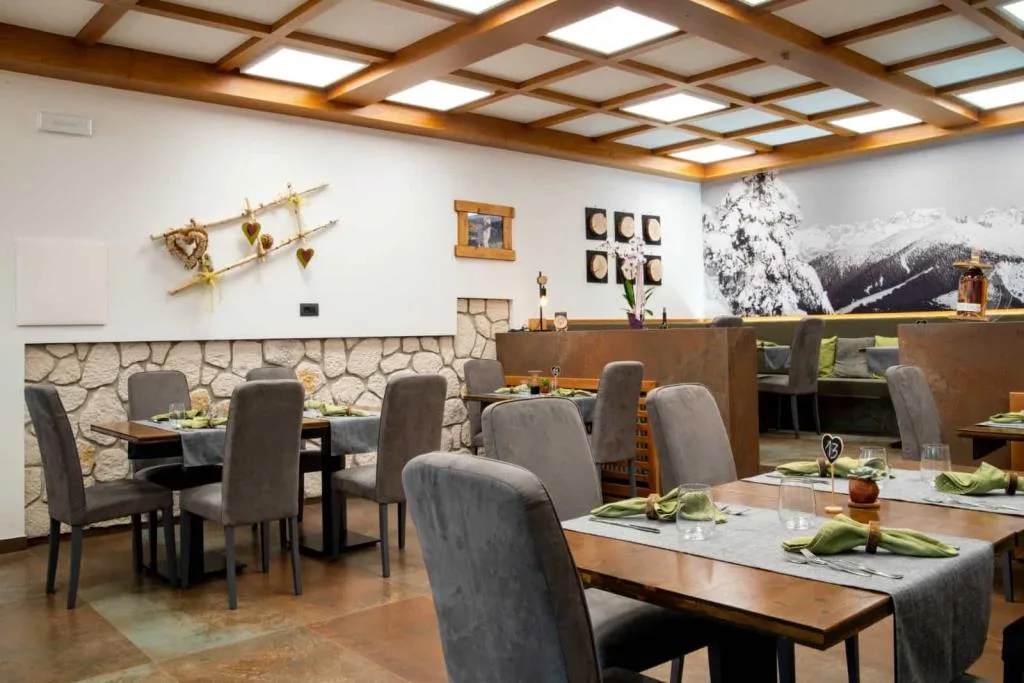 Ristorante elegante con parete in pietra, tavoli in legno e murale delle Dolomiti