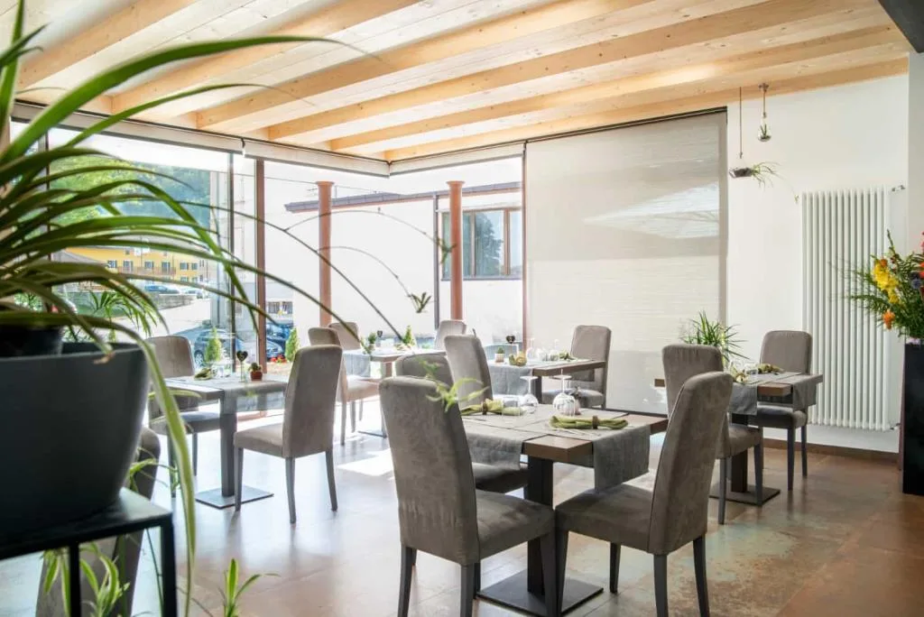 Sala da pranzo luminosa con grandi vetrate, piante e tavoli apparecchiati