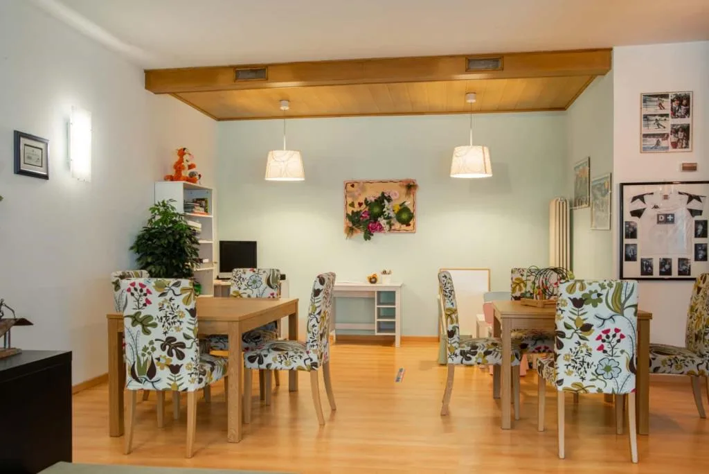 Sala comune con tavoli in legno e sedie rivestite a fantasia floreale