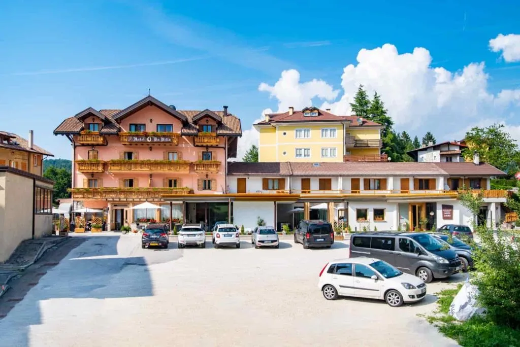 Vista frontale dell'hotel con piazzale, auto parcheggiate e cielo estivo