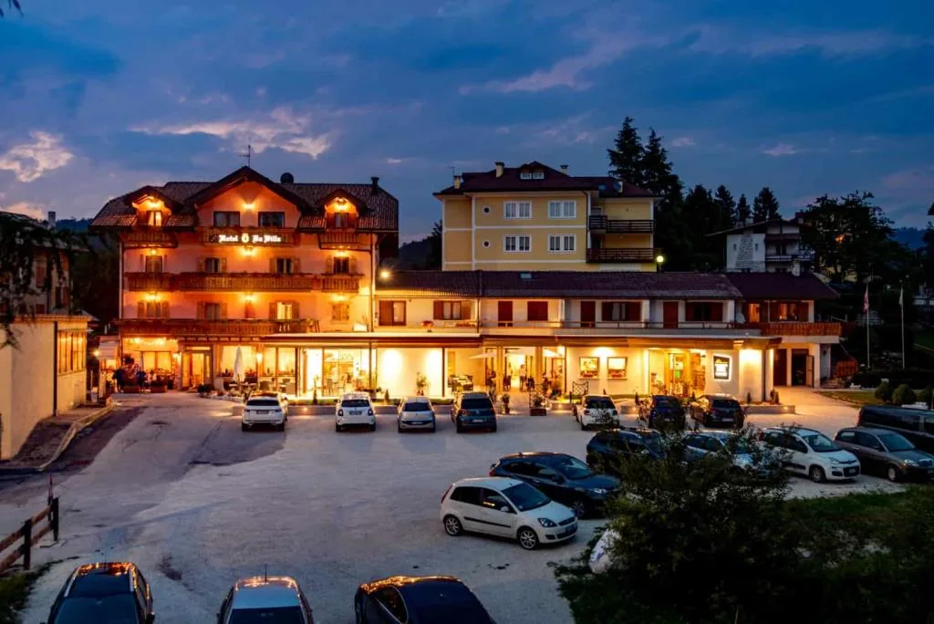 Vista notturna dell'hotel illuminato con ampio piazzale e auto parcheggiate