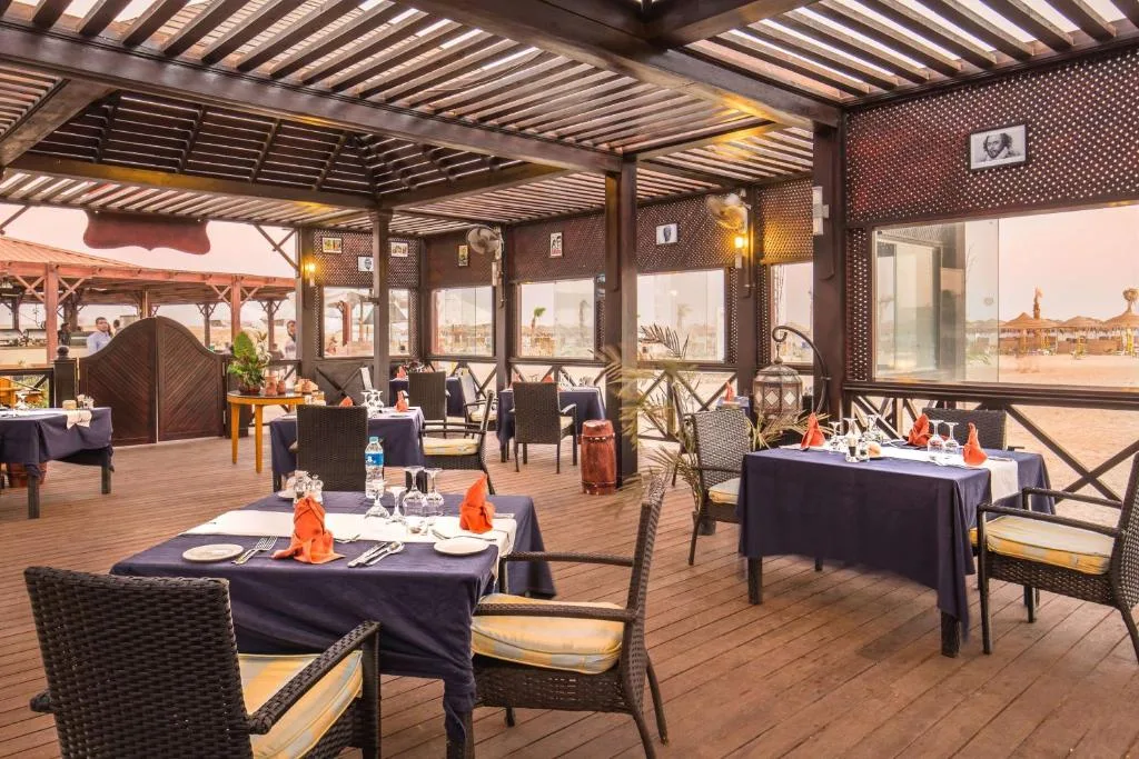 Ristorante sulla spiaggia con pergolato in legno, tavoli con tovaglie blu e vista sulla sabbia al tramonto