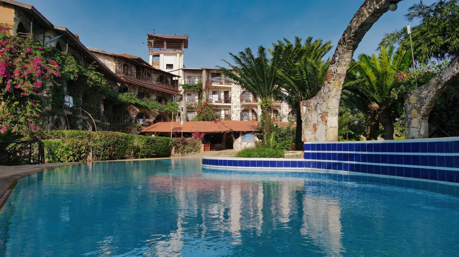 Piscina con bordo in mosaico blu e riflessi dell'edificio in pietra circondato da giardino