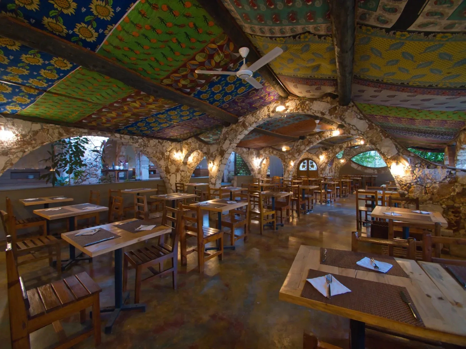 Sala ristorante con soffitto in tessuti colorati a fantasia, archi in pietra e tavoli in legno apparecchiati