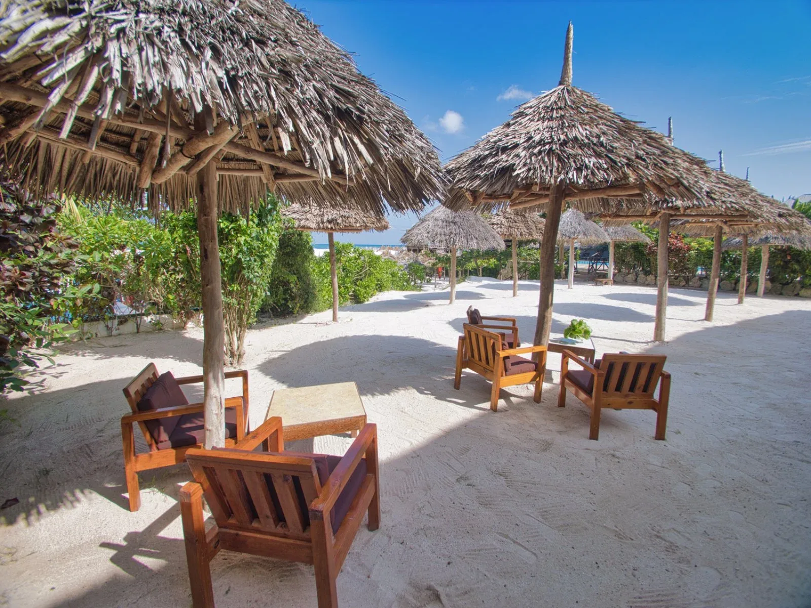Area relax sulla spiaggia con poltrone in legno e ombrelloni in paglia sulla sabbia bianca